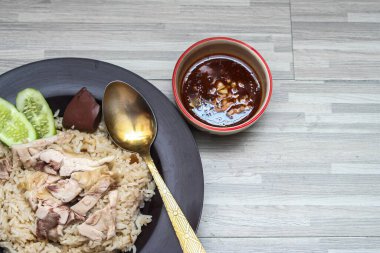 chicken rice with rich broth-infused grains, cucumber slices, and congealed bloodserved with golden utensils on a rustic wooden table.