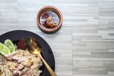 chicken rice with rich broth-infused grains, cucumber slices, and congealed bloodserved with golden utensils on a rustic wooden table.