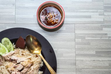 chicken rice with rich broth-infused grains, cucumber slices, and congealed bloodserved with golden utensils on a rustic wooden table.
