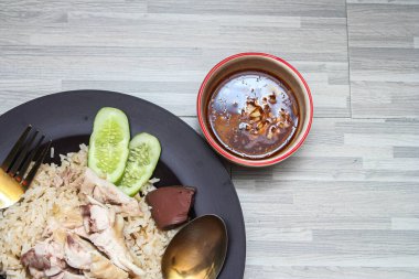 chicken rice with rich broth-infused grains, cucumber slices, and congealed bloodserved with golden utensils on a rustic wooden table.le.