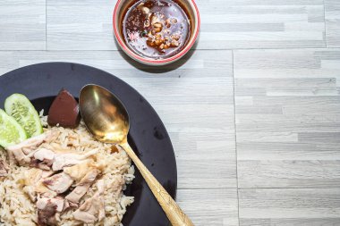 chicken rice with rich broth-infused grains, cucumber slices, and congealed bloodserved with golden utensils on a rustic wooden table.