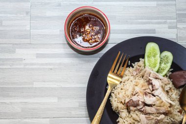 chicken rice with rich broth-infused grains, cucumber slices, and congealed bloodserved with golden utensils on a rustic wooden table.