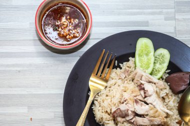 chicken rice with rich broth-infused grains, cucumber slices, and congealed bloodserved with golden utensils on a rustic wooden table.