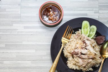 chicken rice with rich broth-infused grains, cucumber slices, and congealed bloodserved with golden utensils on a rustic wooden table.