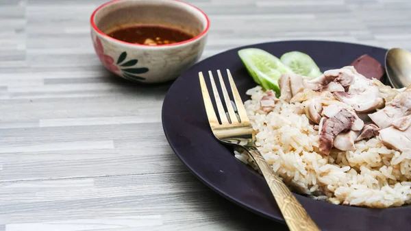 chicken rice with rich broth-infused grains, cucumber slices, and congealed bloodserved with golden utensils on a rustic wooden table.