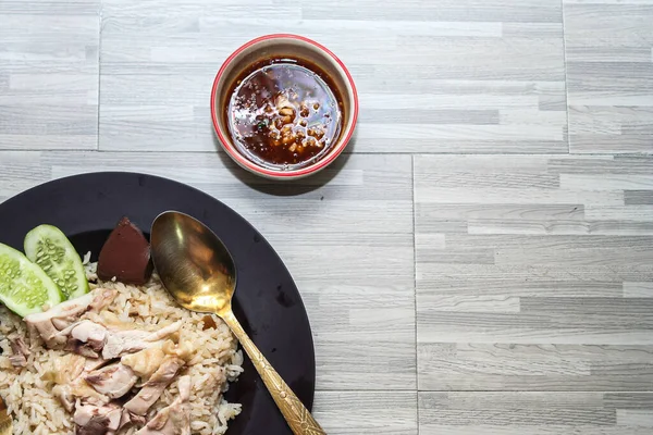chicken rice with rich broth-infused grains, cucumber slices, and congealed bloodserved with golden utensils on a rustic wooden table.