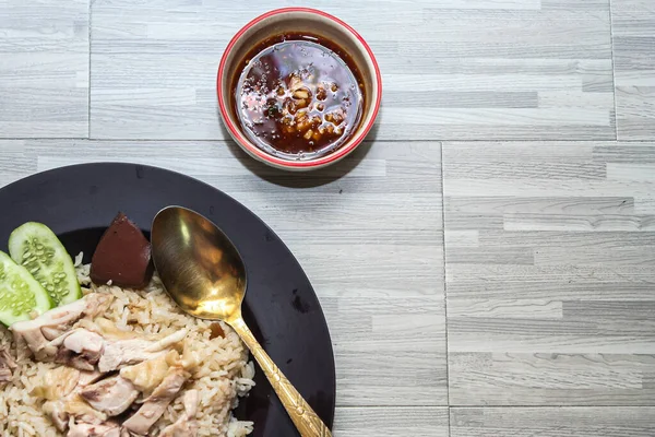 chicken rice with rich broth-infused grains, cucumber slices, and congealed bloodserved with golden utensils on a rustic wooden table.