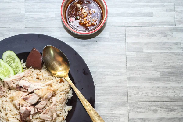 chicken rice with rich broth-infused grains, cucumber slices, and congealed bloodserved with golden utensils on a rustic wooden table.