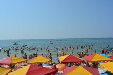 Karadeniz kıyısında turistler ve tatilcilerin olduğu parlak kırmızı plaj şemsiyeleri.