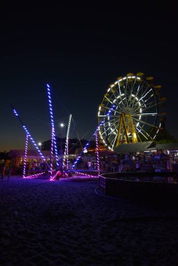 Gece eğlence ve aktiviteler, beyaz dönme dolap, bir ışık, mavi, sarı renk ve bir çocuk havuzu ile trambolin ile Karadeniz'in Plaj rahatlama.