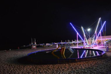 Bir çocuk havuzu, diyot şeritler ve kıyı boyunca plaj şemsiyeleri ile giyinmiş bir trambolin ile Karadeniz'in sahilde gece dinlenme