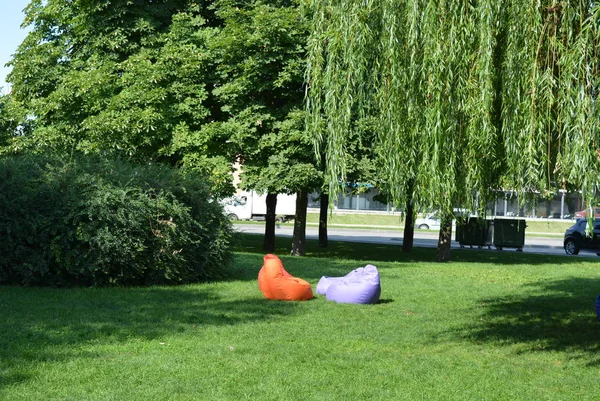 The recreation area, on the green lawn among green trees and bushes, are multi-colored pillows for rest and relaxation in the sun and in the shade