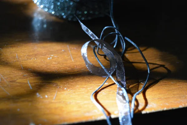Metal sponge with a transparent black ribbon and black threads on a brown wooden table with rays of the sun