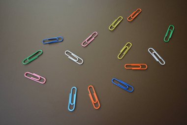 Farklı renklerdeki klipler dağınık ve çok renkli klipler kahverengi bir mat arkaplan üzerine yayılmış.