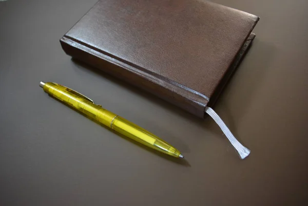 Brown book diary with a yellow pen on a brown matte background.