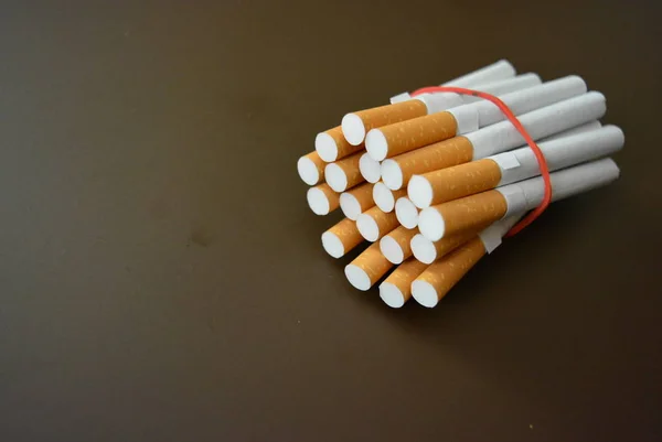 Cigarettes from the pack are fixed with a red rubber band on a brown matte background.