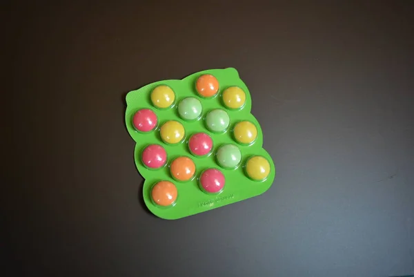 Bright green plate of baby vitamin tablets on a matte brown background.