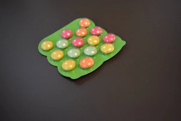 Bright green plate of baby vitamin tablets on a matte brown background.