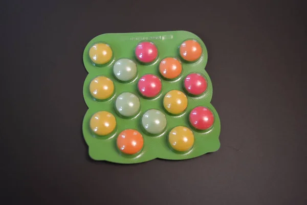 Bright green plate of baby vitamin tablets on a matte brown background.