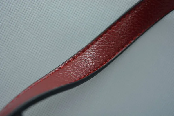Cherry red belt, genuine cowhide leather strap with metal carbines on a white fabric photo background.