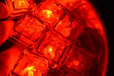 Plastik parlayan parlak kırmızı buz küpleri suda. Kırmızı buz kütleleri ilginç bir metal yansıması ile paslanmaz çelik dipper yüzen vardır. Kırmızı nokta aydınlatmalı kırmızı su arka planı.