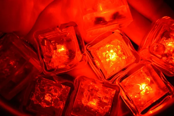 Plastic glowing bright red ice cubes in water. Red ice floes are floating in a stainless steel dipper with an interesting metal reflection. Red water background with red spot lighting.