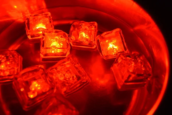 Plastic glowing bright red ice cubes in water. Red ice floes are floating in a stainless steel dipper with an interesting metal reflection. Red water background with red spot lighting.