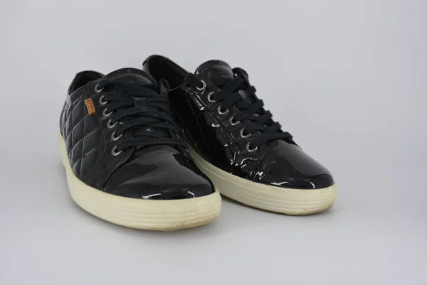 Youth black patent leather shoes, sneakers with a thick white sole and black laces. Stylish and elegant shoes with an interesting style and material located on a white background.