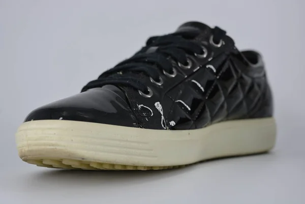 Youth black patent leather shoes, sneakers with a thick white sole and black laces. Stylish and elegant shoes with an interesting style and material located on a white background.