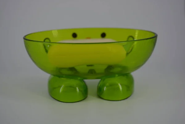 Bright green transparent soap dish with cosmetic soap is located on a white background. Positive soap dish with a smile, cheerful and good mood.