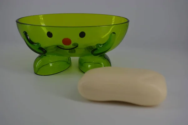 Bright green transparent soap dish with cosmetic soap is located on a white background. Positive soap dish with a smile, cheerful and good mood.