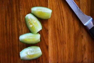 Bir metal mutfak bıçağı ile bir yaz salatası için yeşil taze dilimlenmiş salatalık kahverengi ahşap mutfak tahtası üzerinde yalan.