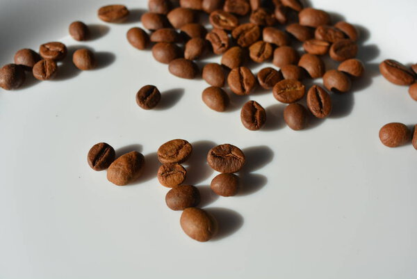 On a white glass plate spilled chaotically coffee beans laid delicious grains throughout the plate.