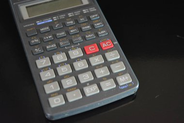 Siyah parlak arka plan üzerinde bulunan güzel renklerile kaliteli plastikten yapılmış gri bir hesap makinesi.