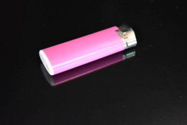 Pembe plastik çakmak parlak siyah bir yüzey üzerinde yatıyor.