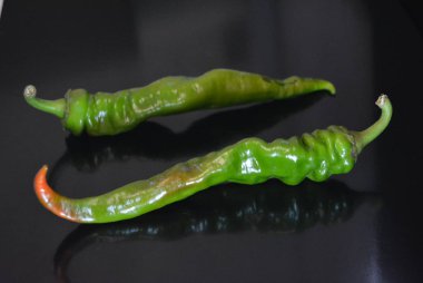 Taze sulu yeşil acı biber, tekrarlanan yansıması ile siyah parlak bir yüzey üzerinde yatan iki biber.