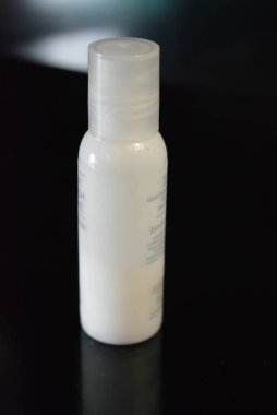 Vücut ve güzellik bakımı için kozmetik ve tıbbi ürünler ile beyaz küçük plastik şişe parlak siyah bir yüzey üzerinde.