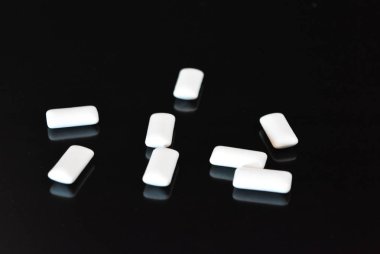 Beyaz lezzetli yastıklar, siyah parlak bir yüzey üzerinde bulunan sakız yastıklar.