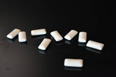 Beyaz lezzetli yastıklar, siyah parlak bir yüzey üzerinde bulunan sakız yastıklar.