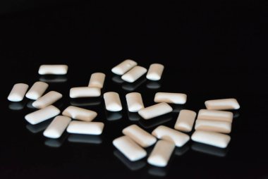 Beyaz lezzetli yastıklar, siyah parlak bir yüzey üzerinde bulunan sakız yastıklar.