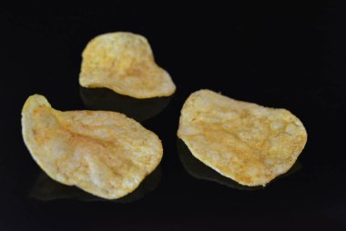 Ambalajından lezzetli, gevrek patates cipsi yansımaile siyah parlak bir yüzey üzerinde yalan.