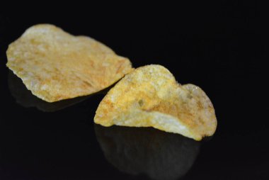 Ambalajından lezzetli, gevrek patates cipsi yansımaile siyah parlak bir yüzey üzerinde yalan.