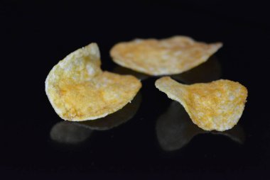 Ambalajından lezzetli, gevrek patates cipsi yansımaile siyah parlak bir yüzey üzerinde yalan.