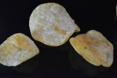 Ambalajından lezzetli, gevrek patates cipsi yansımaile siyah parlak bir yüzey üzerinde yalan.