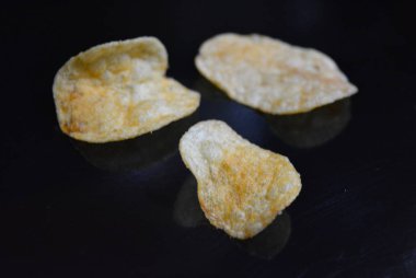 Ambalajından lezzetli, gevrek patates cipsi yansımaile siyah parlak bir yüzey üzerinde yalan.