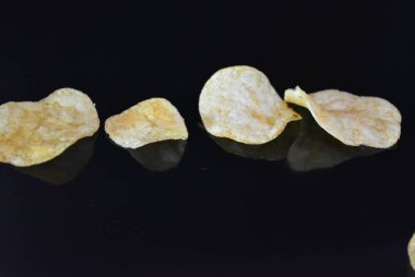Ambalajından lezzetli, gevrek patates cipsi yansımaile siyah parlak bir yüzey üzerinde yalan.