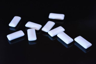 Beyaz lezzetli yastıklar, siyah parlak bir yüzey üzerinde bulunan sakız yastıklar.