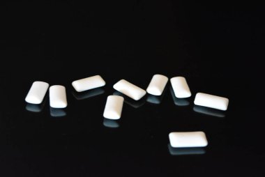 Beyaz lezzetli yastıklar, siyah parlak bir yüzey üzerinde bulunan sakız yastıklar.