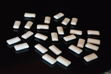 Beyaz lezzetli yastıklar, siyah parlak bir yüzey üzerinde bulunan sakız yastıklar.