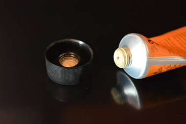 Parlak siyah bir yüzey üzerinde bulunan bir kapak ile metal bir tüp yüz ve vücut cilt bakımı için açık bir kozmetik krem.